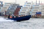 People ride on a boat past A.P. Moeller-Maersk A/S branded shipping containers stacked at the Ladol free trade zone port in Lagos, Nigeria.