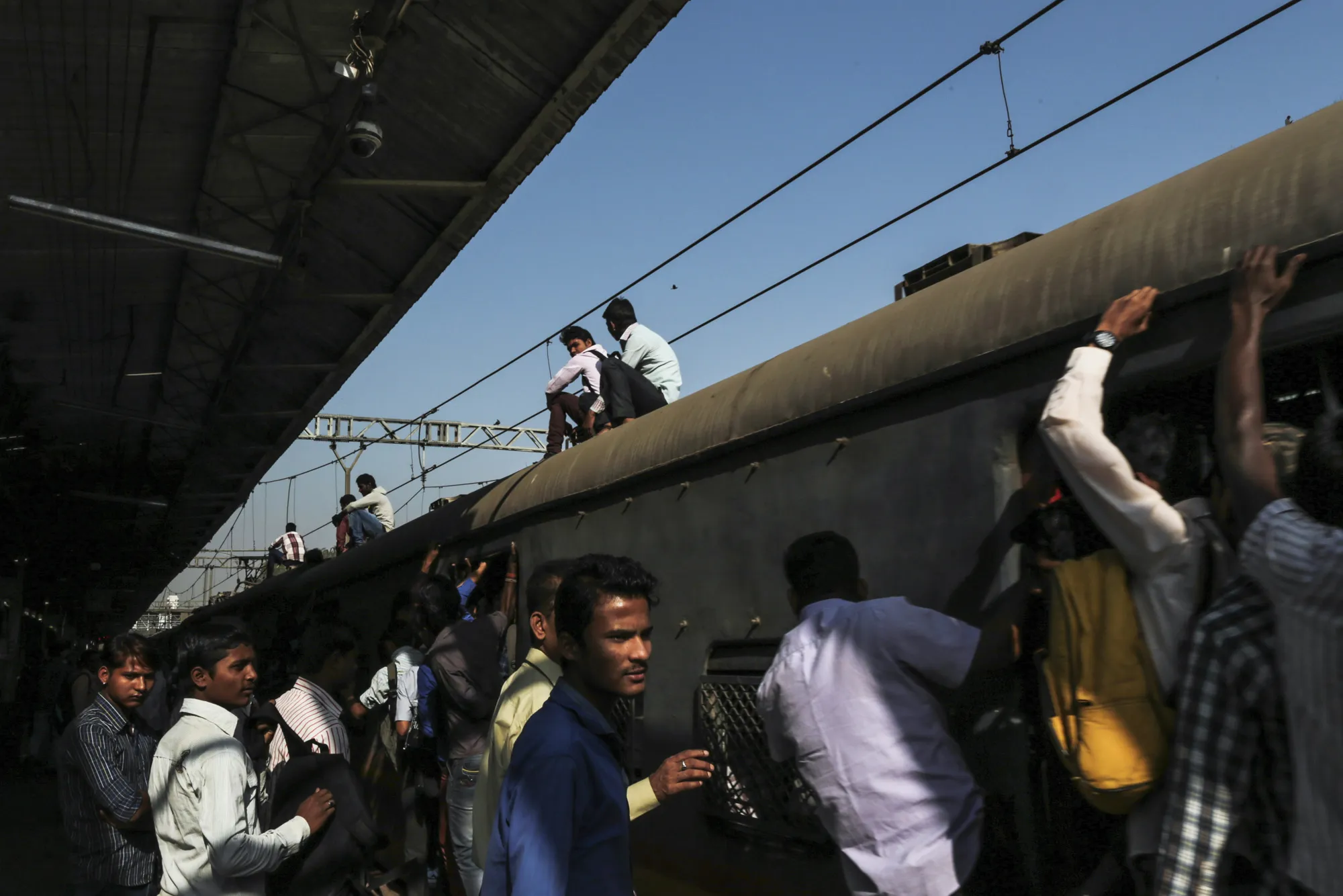 Passengers wait to board a train as others ride on the roof at Tilak Nagar railway station in Mumbai.