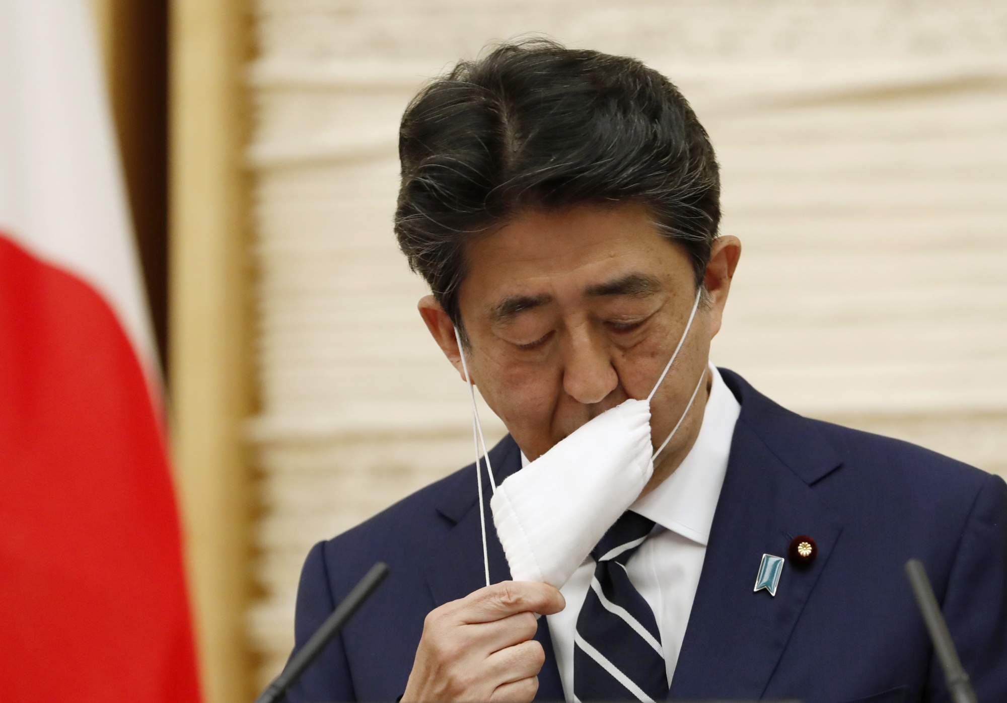 Shinzo Abe takes off his protective mas during a news conference in Tokyo.