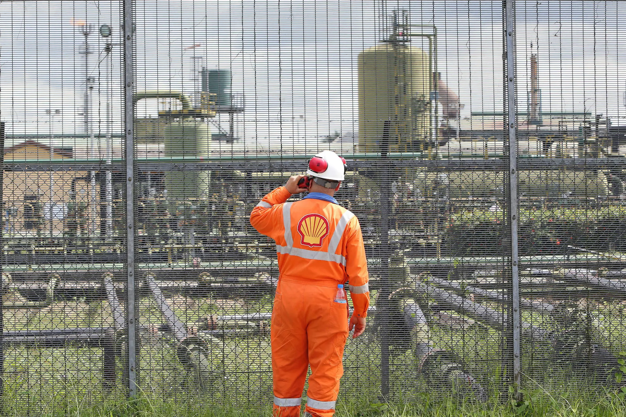 An employee speaks on a radio at the perimeter security fence of the Agbada oil flow station, operated by Shell Petroleum.

