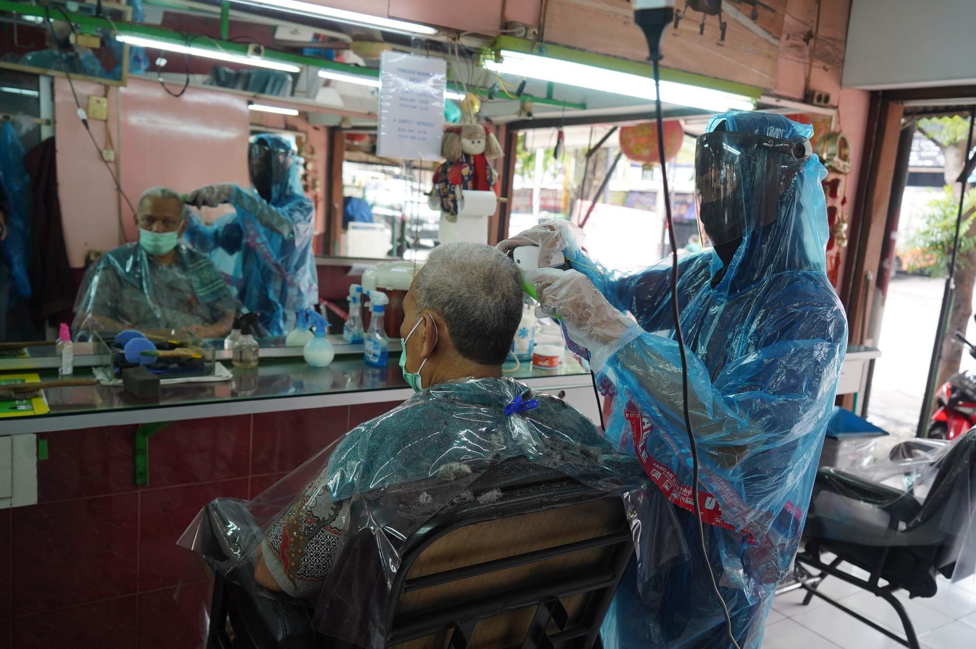 A barber in protective gear cuts a customer's hair in Jakarta, April 28.