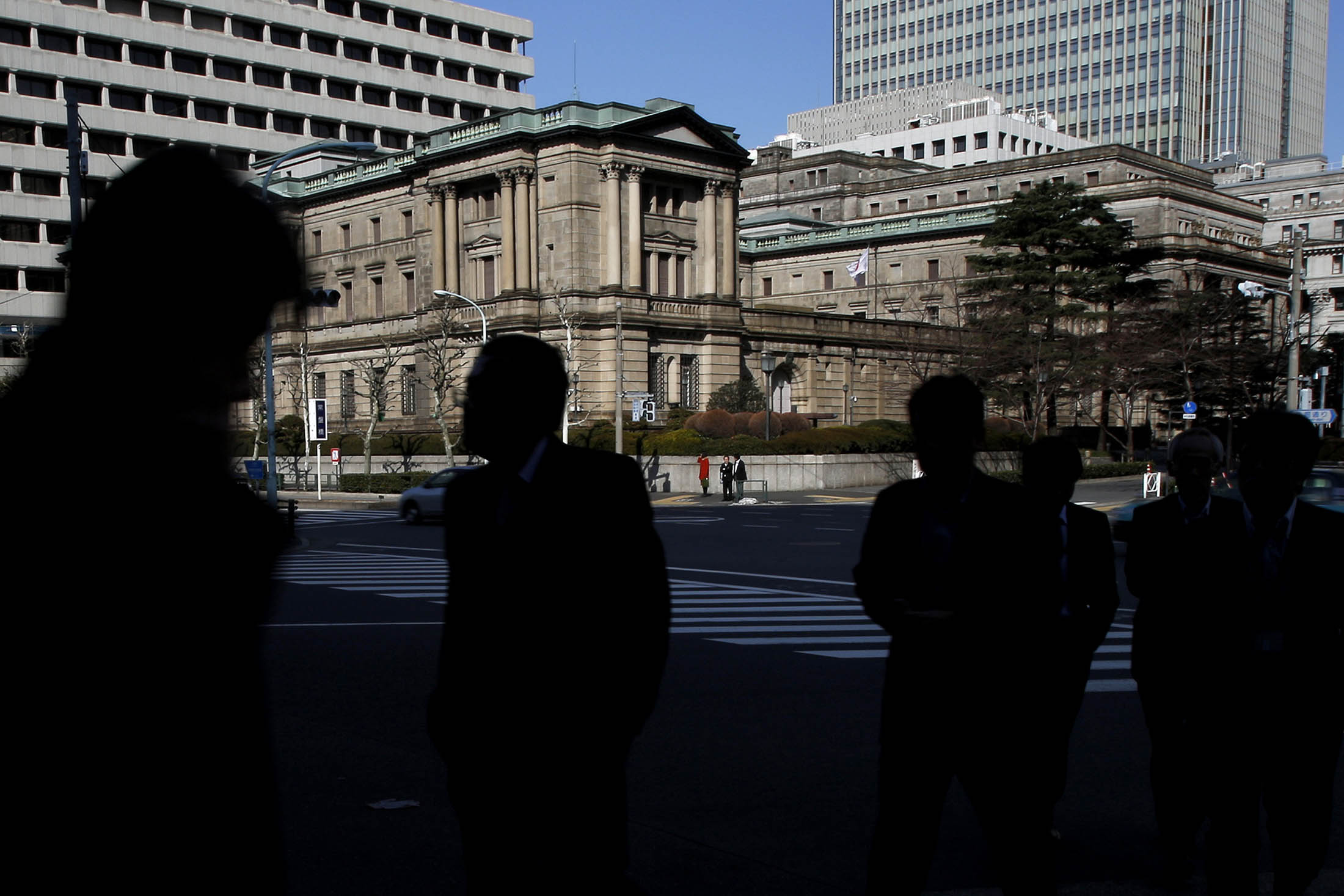 Pedestrians walk in front of the Bank of Japan headquarters in Tokyo, Japan, on Tuesday, Feb. 18, 2014. The Bank of Japan boosted lending programs while sticking with a plan for unprecedented asset purchases, as the central bank tries to support a recovery and stamp out 15 years of deflation.
