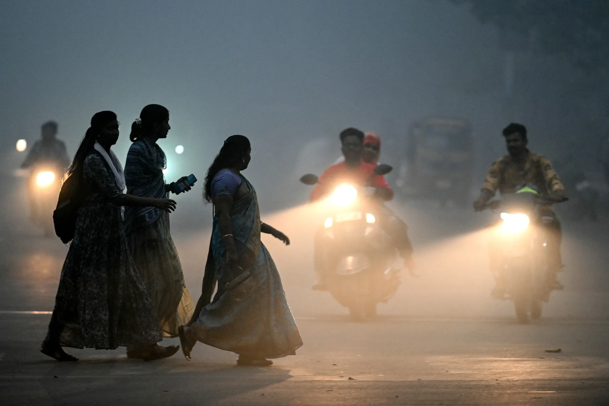 Women walk across a street engulfed by dense smog in Chennai.