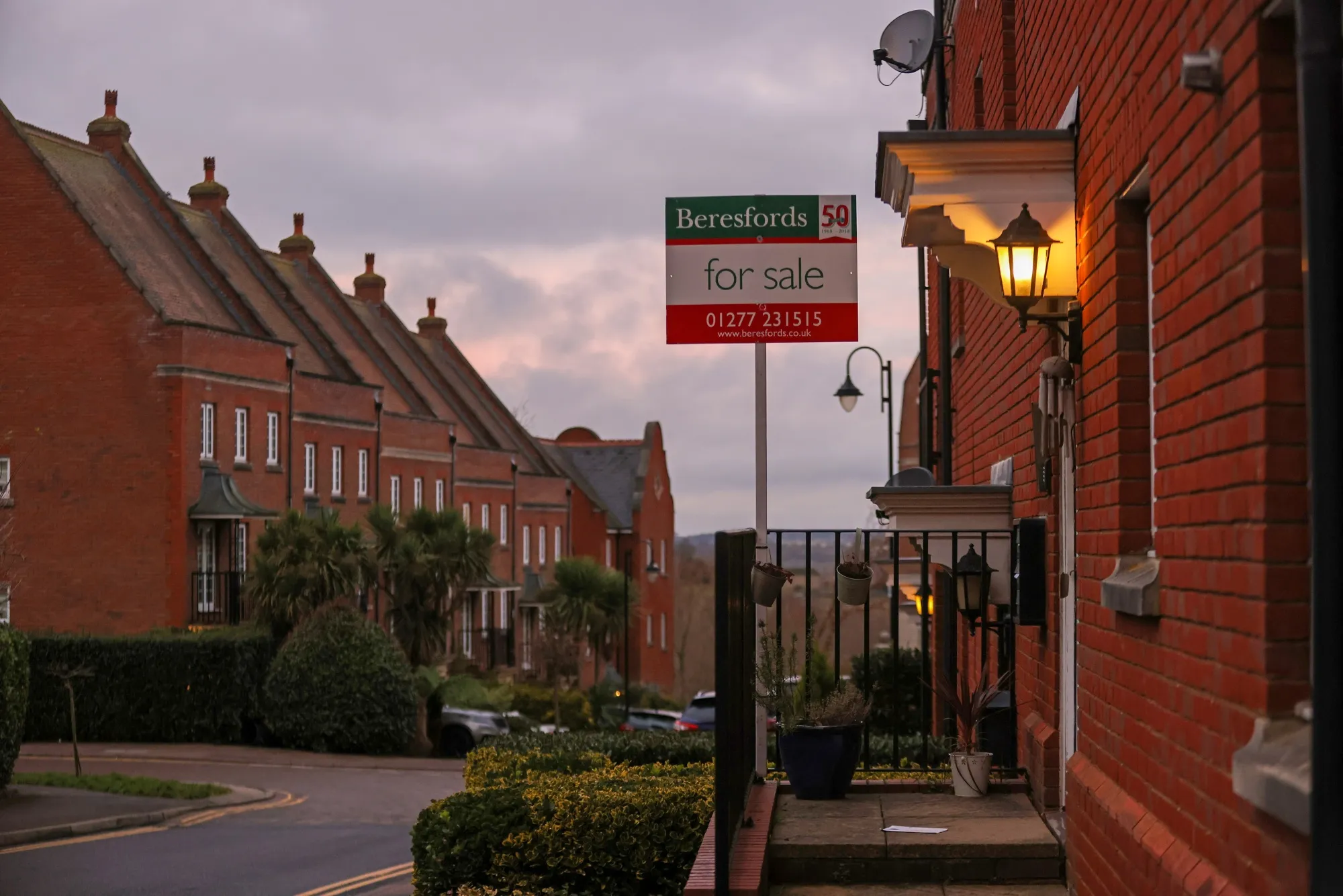 An estate agent's board with a For Sale sign attached outside a residential house in Brentwood, U.K.