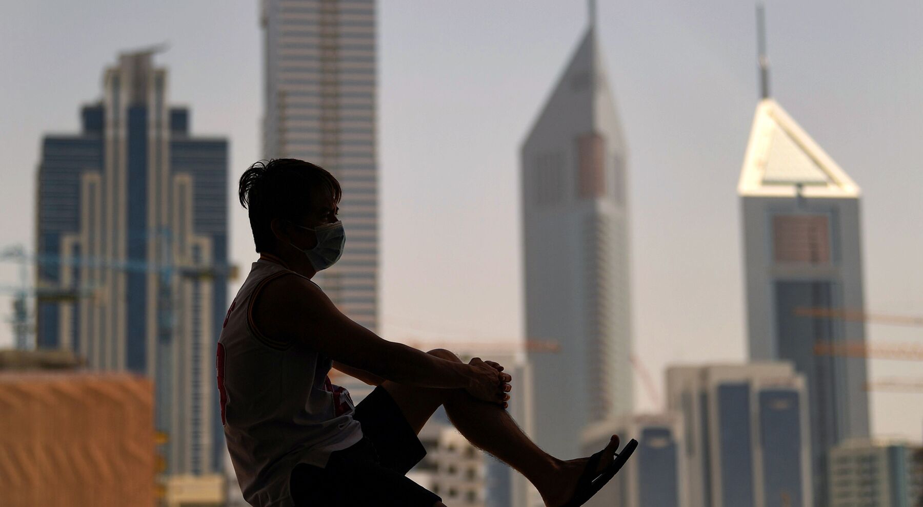  A man wearing a face mask gazes at the Dubai skyline from a window, during a lockdown imposed by the authorities in a bid to slow down the spread of the novel coronavirus in the Emirati city on April 5, 2020. - 