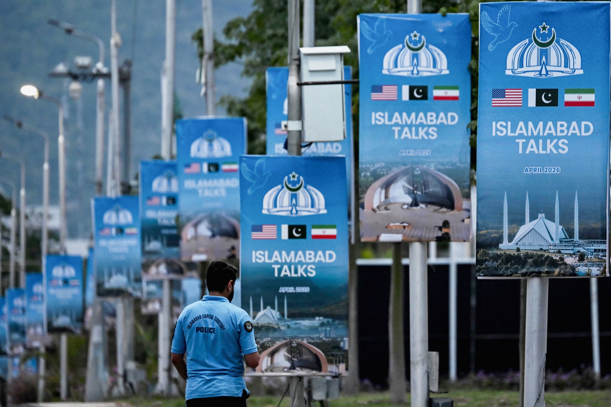 A police personnel walks past posters highlighting Pakistan's mediation of IranUS peace talks, at the Red Zone area in Islamabad on April 18, 2026. No date has been set for the next round of IranUS peace talks brokered by Pakistan following the failure of an initial round, Iran's deputy foreign minister said on April 18. Pakistan's powerful military chief and prime minister concluded separate visits aimed at ending the Iran war, with Field Marshal Asim Munir leaving Tehran and premier Shehbaz Sharif headed home from Turkey. (Photo by Farooq NAEEM / AFP via Getty Images)
