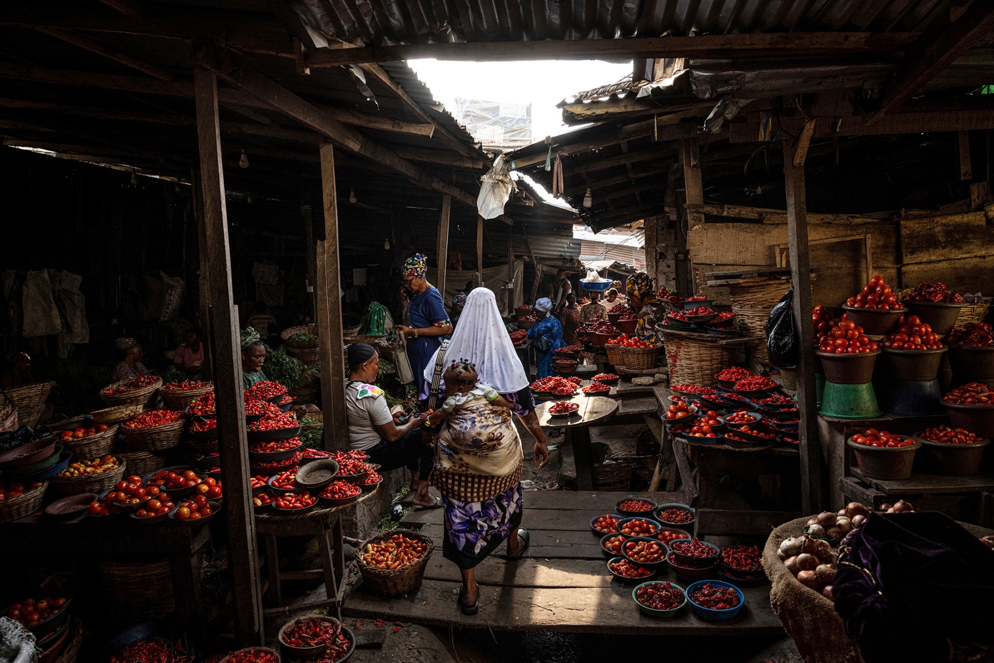 Vendors selling tomatoes and produce in a crowded food market in Lagos, Nigeria.