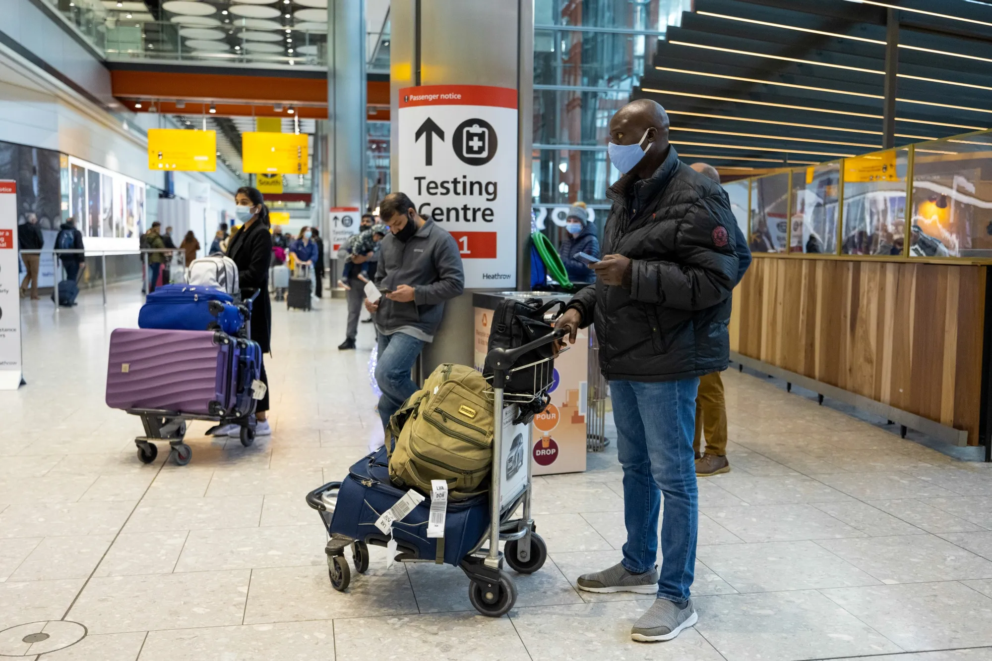 Passengers stand near a sign for a Covid-19 testing centre at London Heathrow Airport Ltd. in London, U.K.