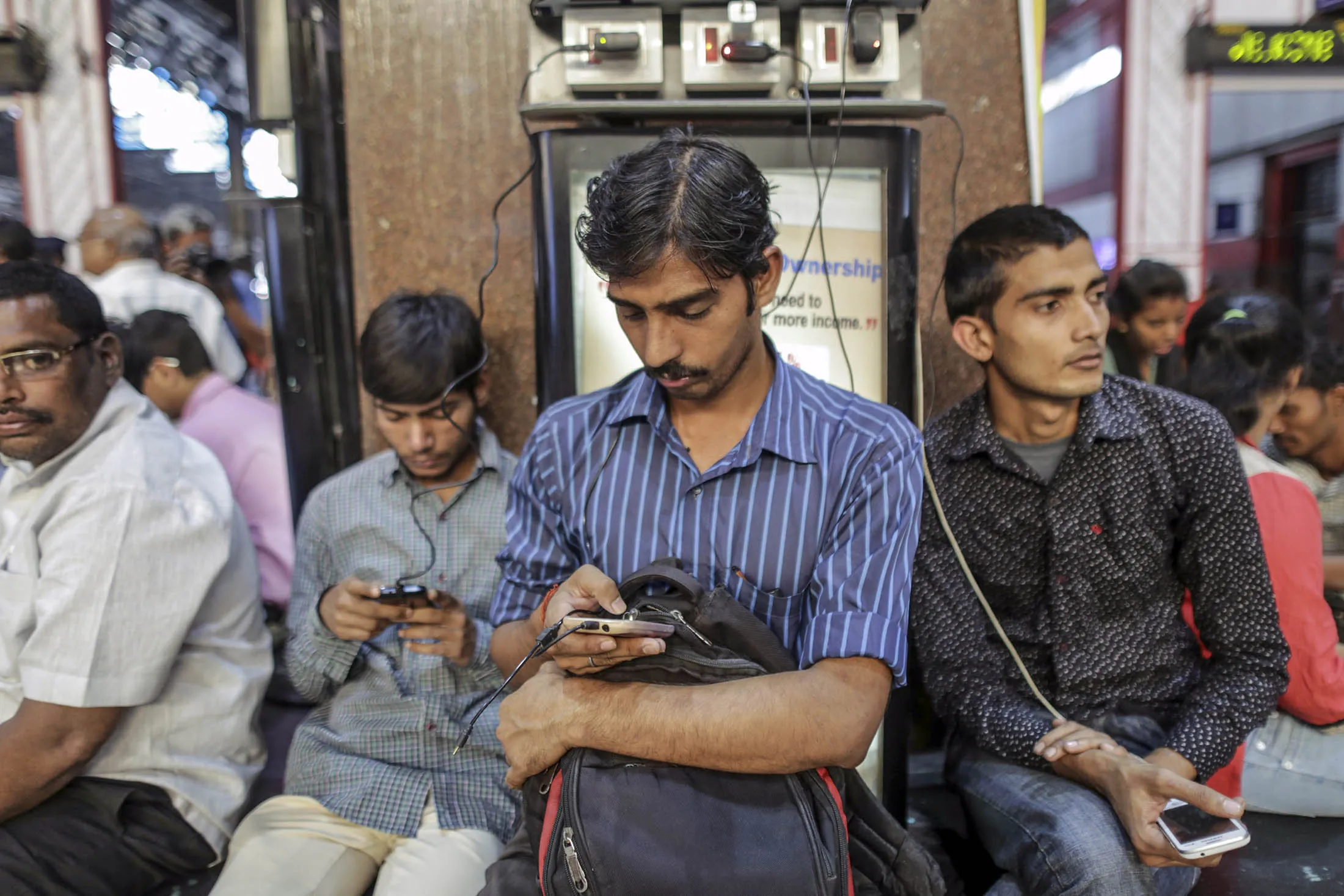 Passengers use smartphones next to a charging station at a railway station in Mumbai. The surging number of mobile devices and people going online through apps for the first time are fueling Asia’s mobile software arena.
