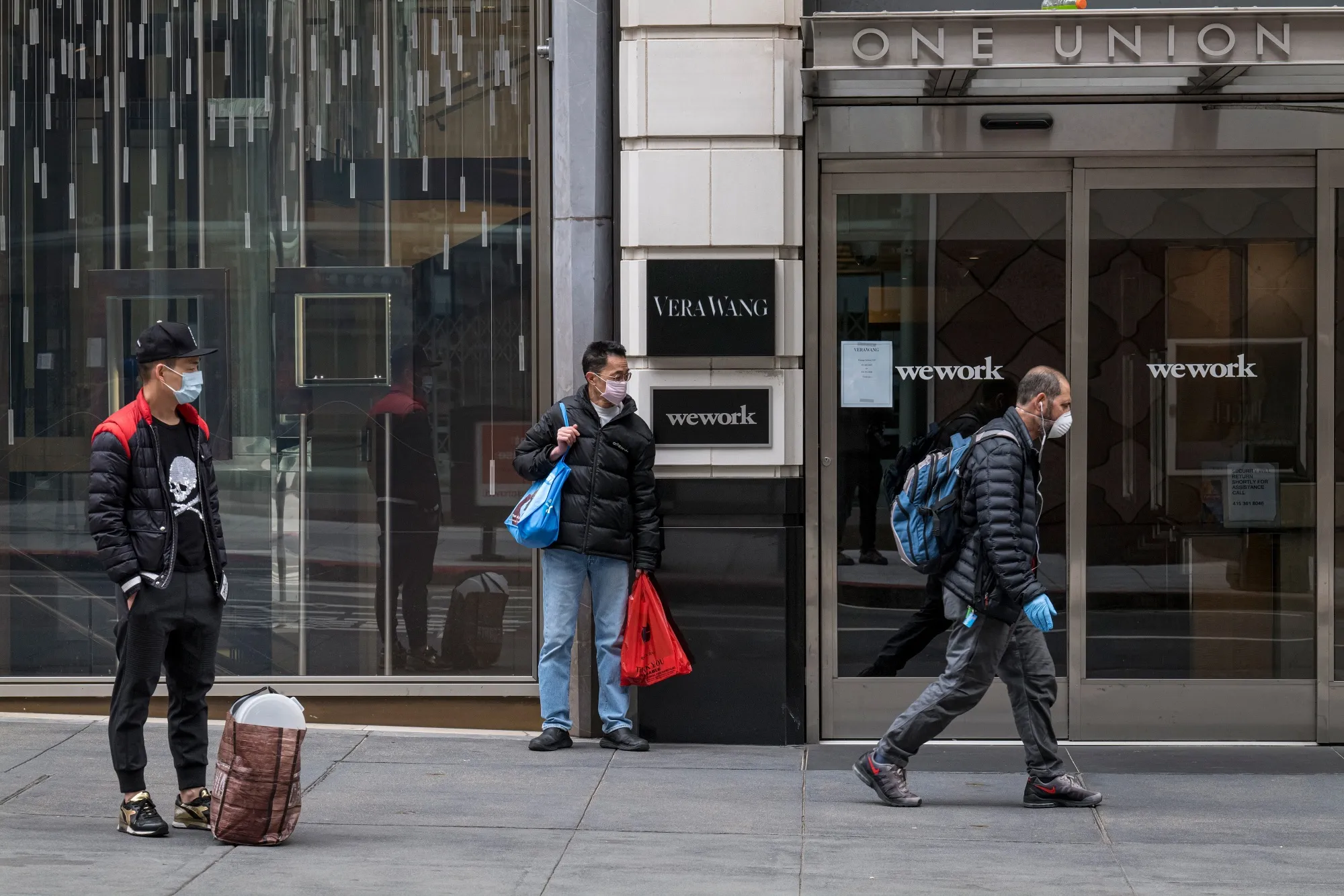 Pedestrians wearing protective face masks stand outside a WeWork location in San Francisco, California, on&nbsp;March 24.&nbsp;