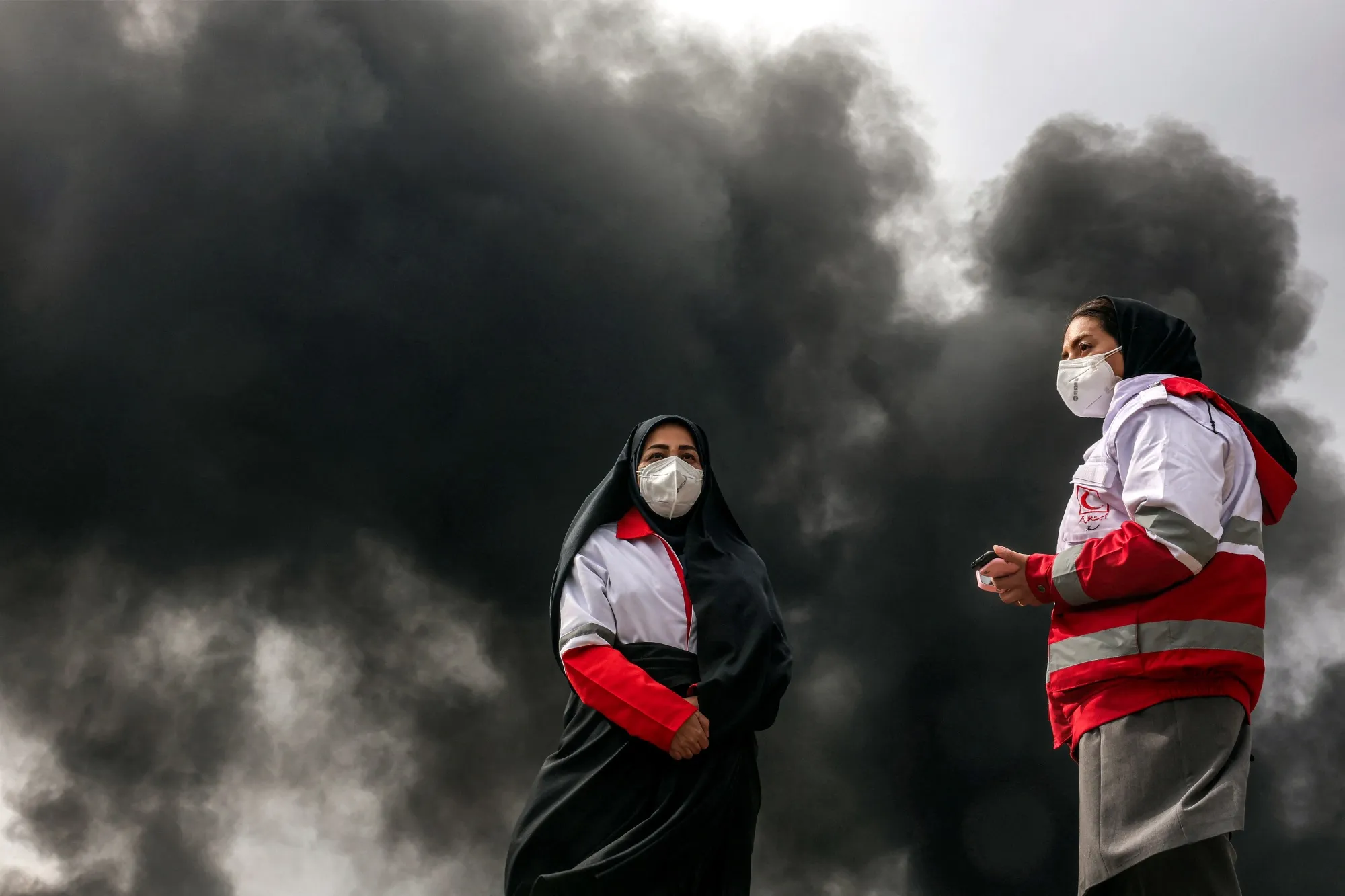 Members of Iran’s Red Crescent society stand near smoke plumes following an overnight airstrike on a refinery earlier this month.