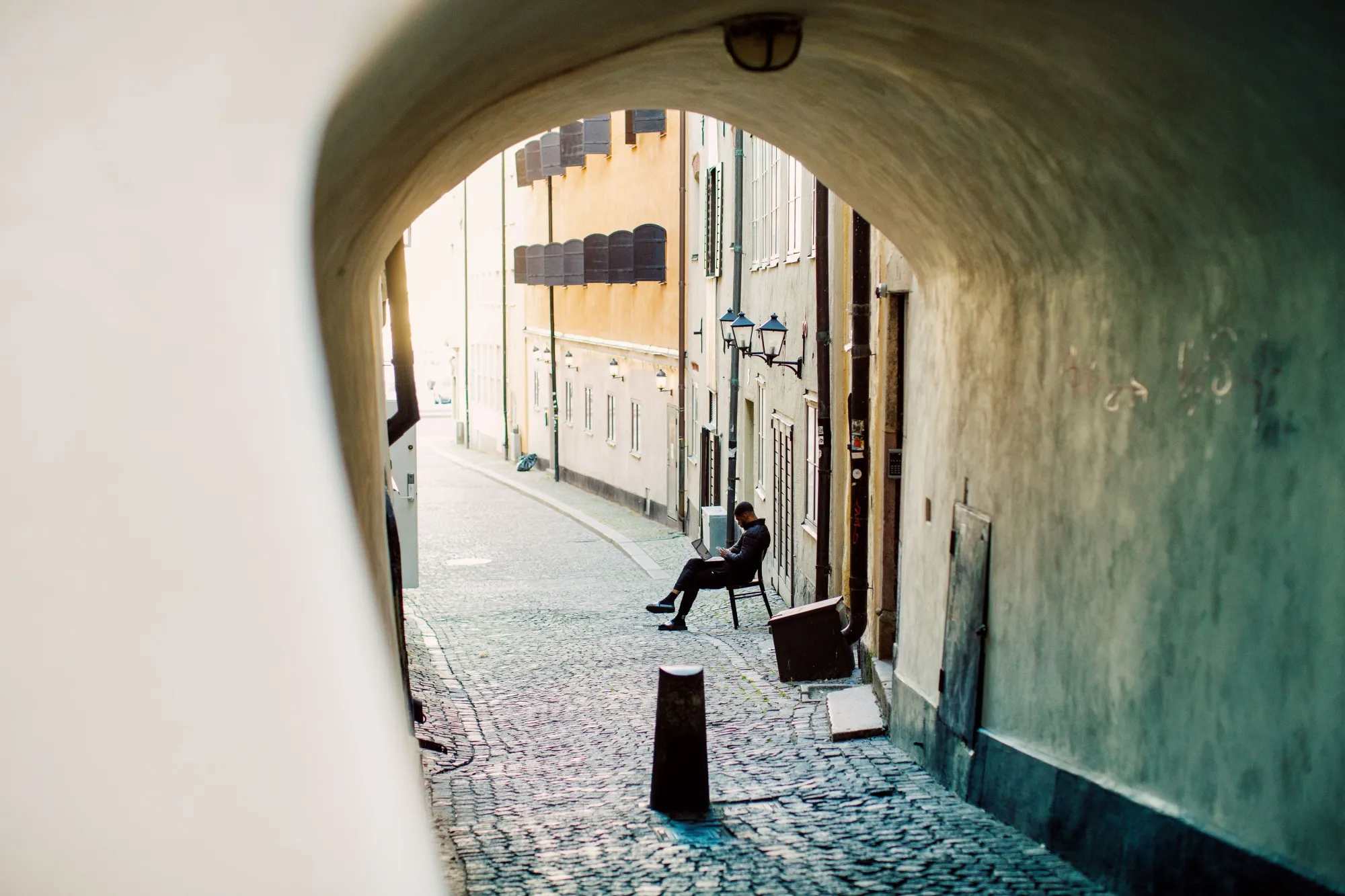 A man works on a laptop outside on a cobbled street in Stockholm.