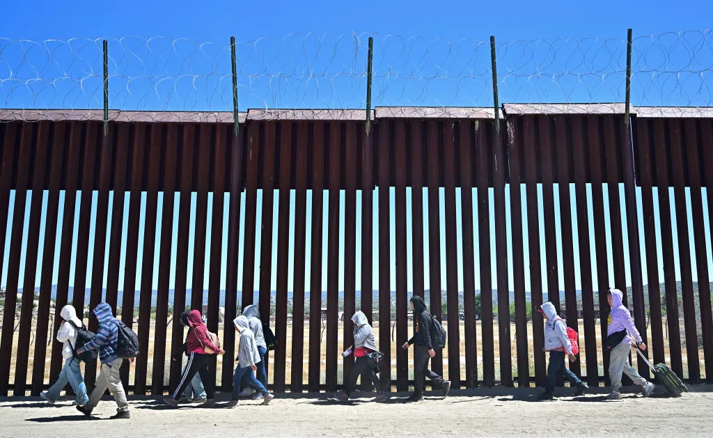 Migrants walk on the US side of the border wall in Jacumba Hot Springs, California. The Trump administration has gutted several programs to oversee children who enter the US alone.&nbsp;