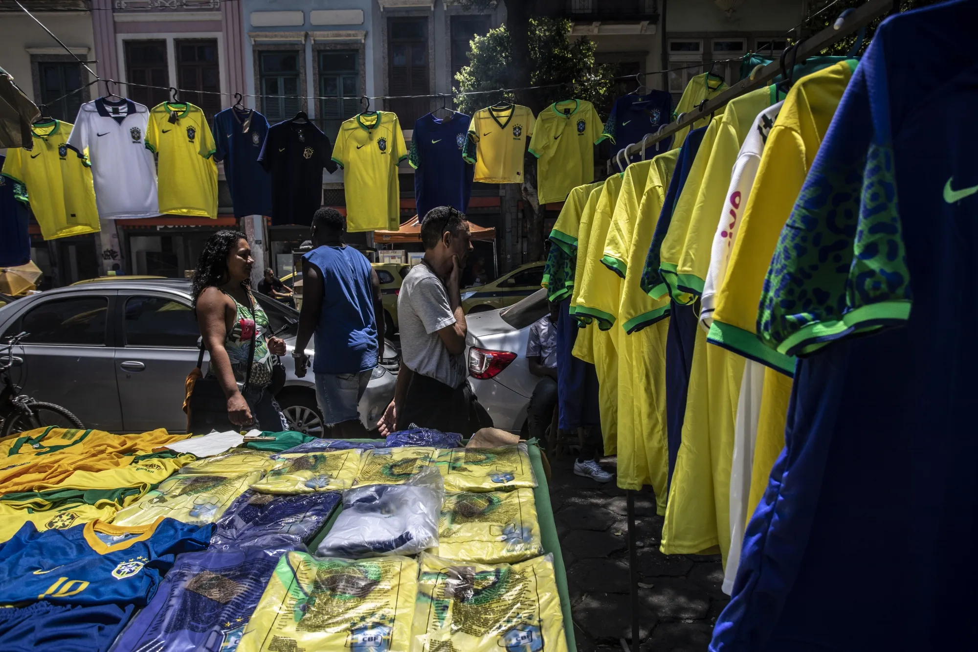 Pedestrians walk past Brazil national team soccer jerseys displayed for sale at a vendor's stand in Rio de Janeiro, Brazil.