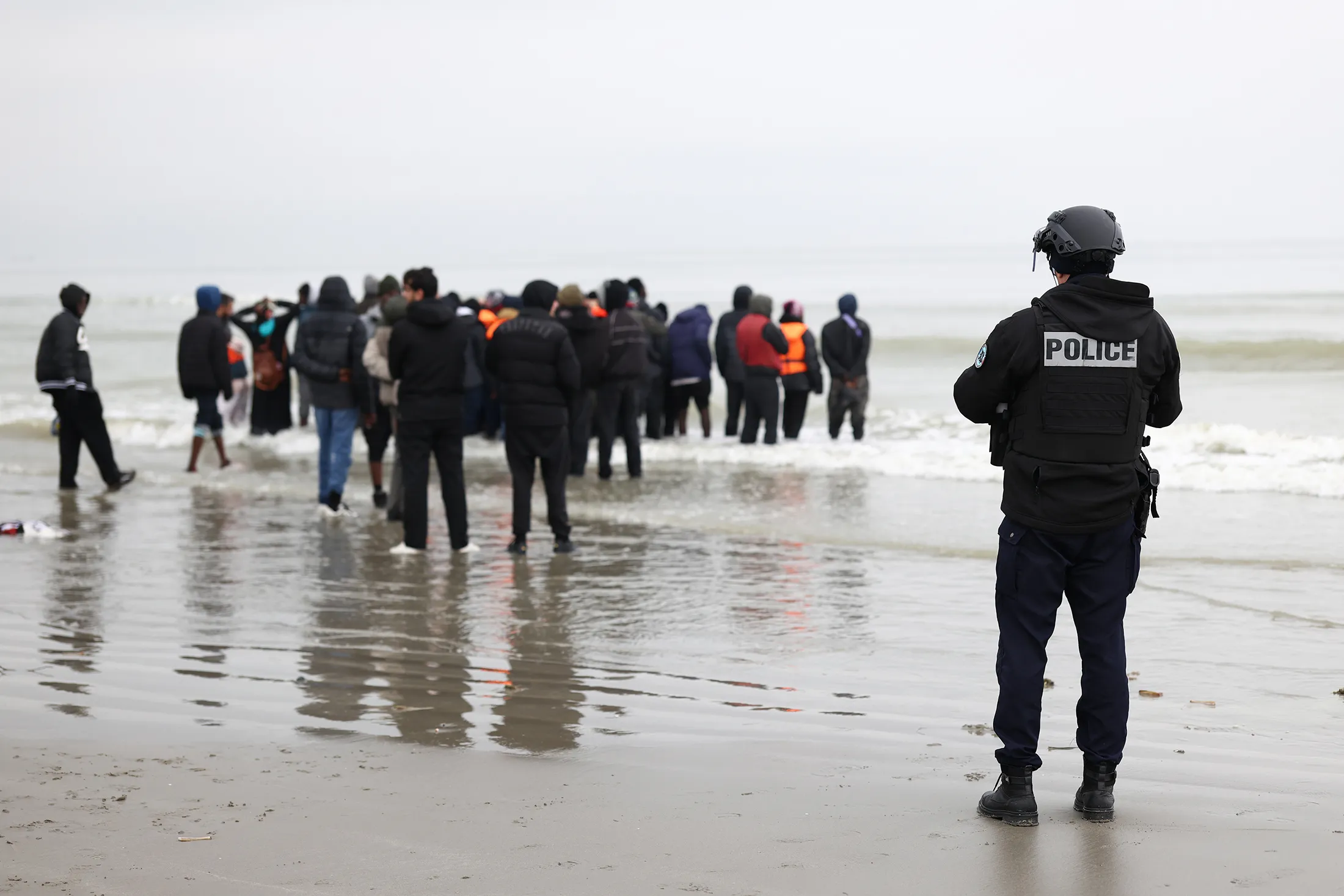 A Police officer watches migrants board a dingy before sailing the English Channel in Gravelines, France.