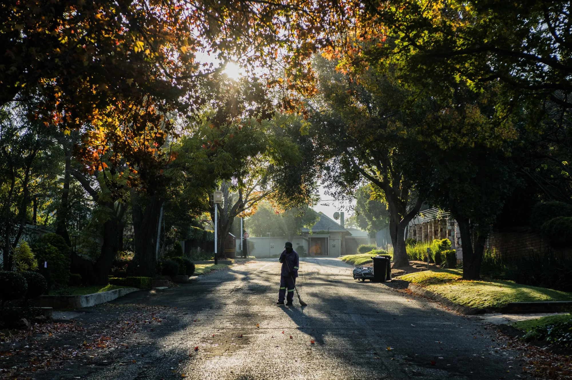 A waste-picker sweeps the road outside residences in a wealthy suburb of Johannesburg.