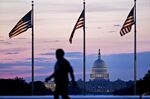 A pedestrian passes in front of American Flags displayed in front of The U.S. Capitol building before sunrise in Washington, D.C.