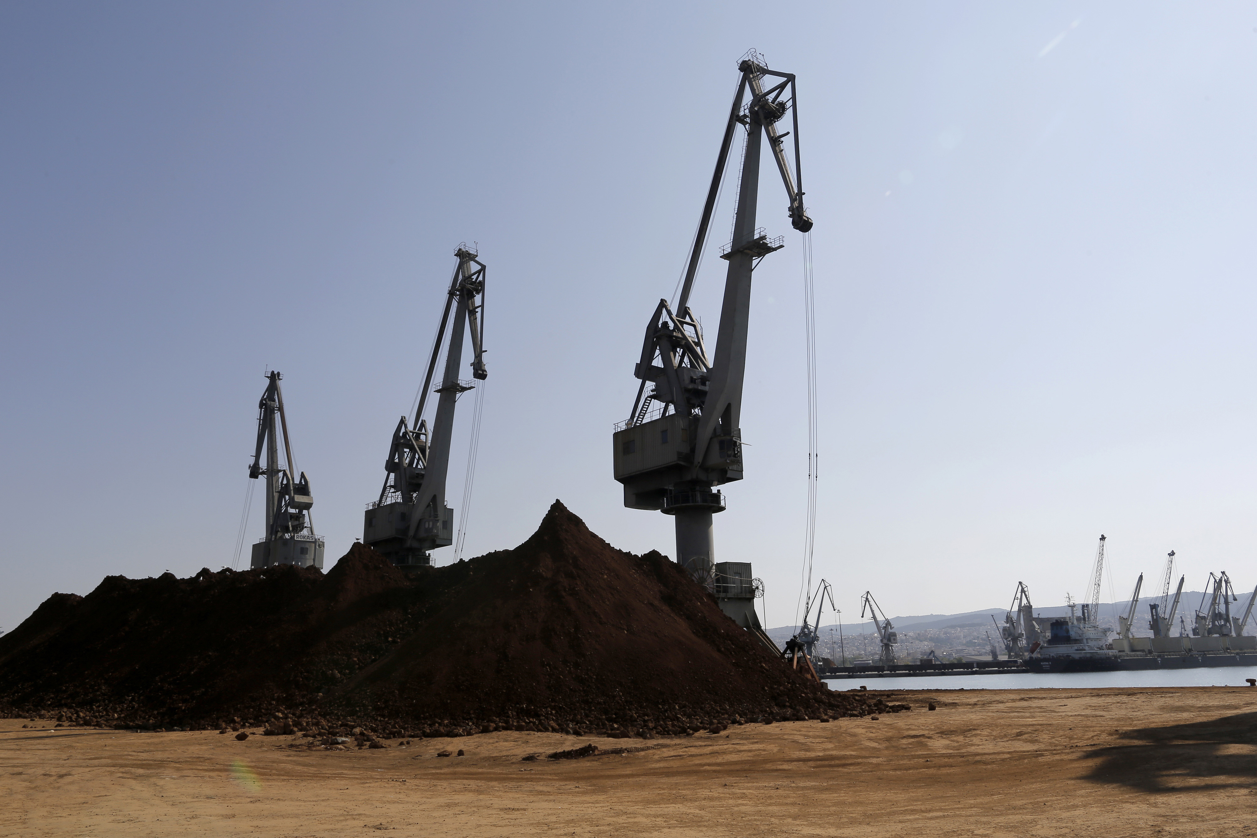 Shipping cranes stand next to supplies of unprocessed nickel ore on the dockside at Thessaloniki port.