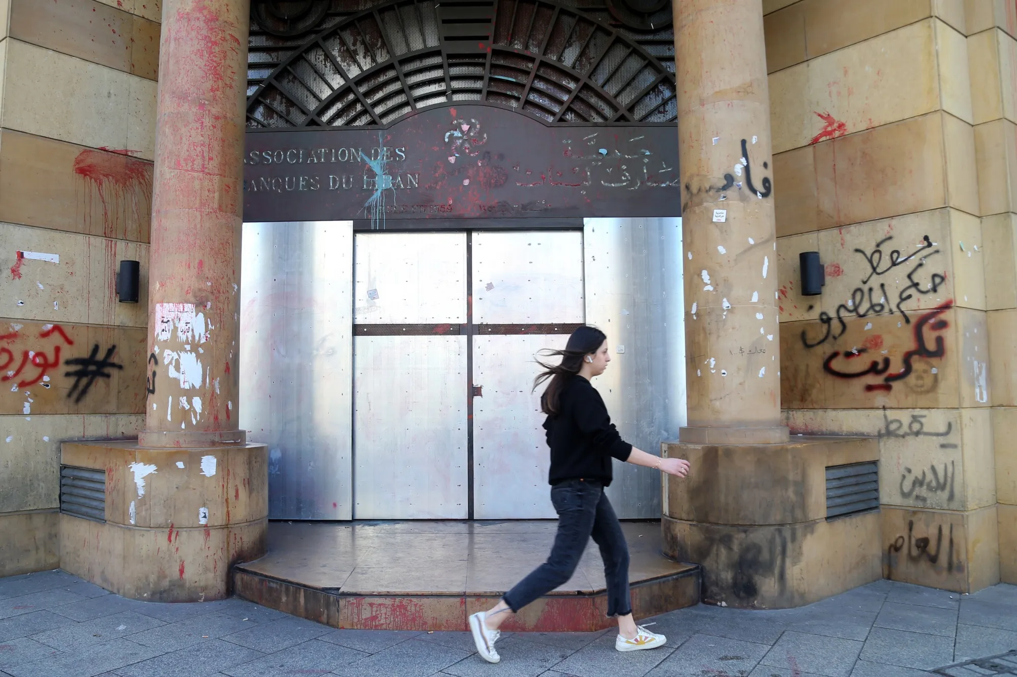 A pedestrian passes metal panels protecting the graffiti covered entrance to the Association of Banks headquarters in Beirut, on March 7.