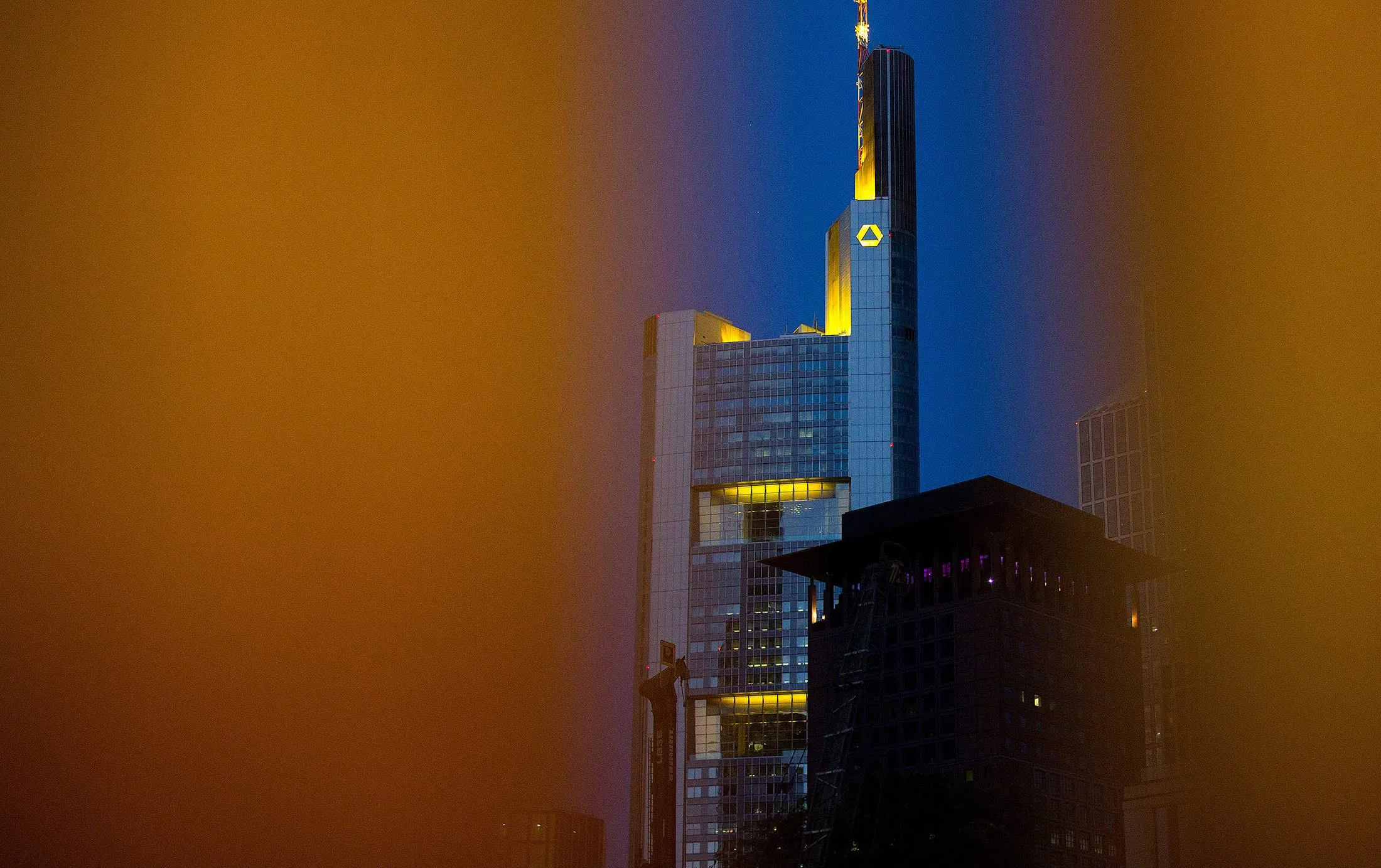 The Commerzbank AG logo sits illuminated on the bank's headquarter offices at dusk in the financial district in Frankfurt.
