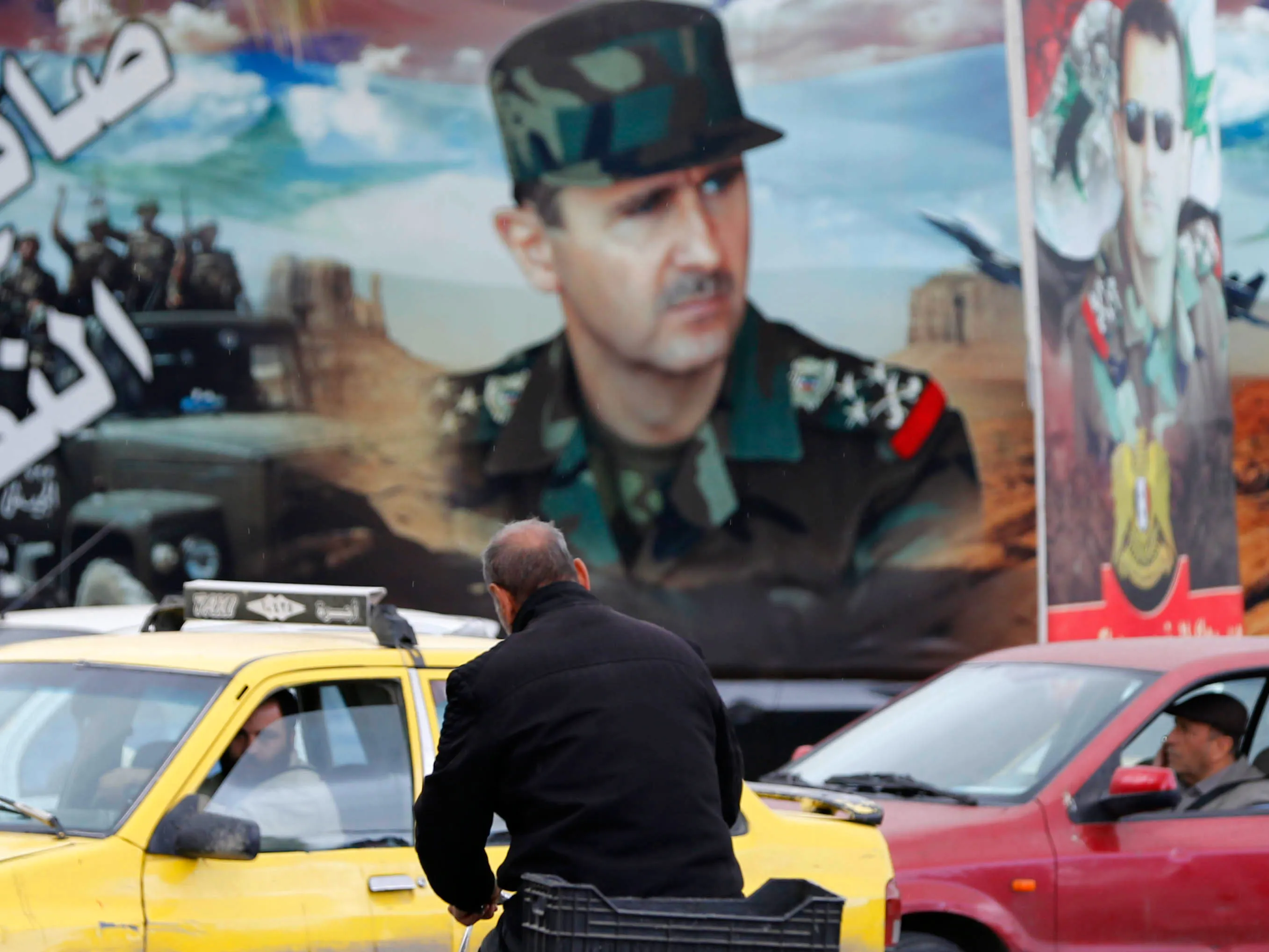 A man rides a bicycle near a portrait of President Bashar al-Assad in Damascus.