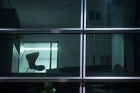 An empty chair sits in an illuminated window of an office block