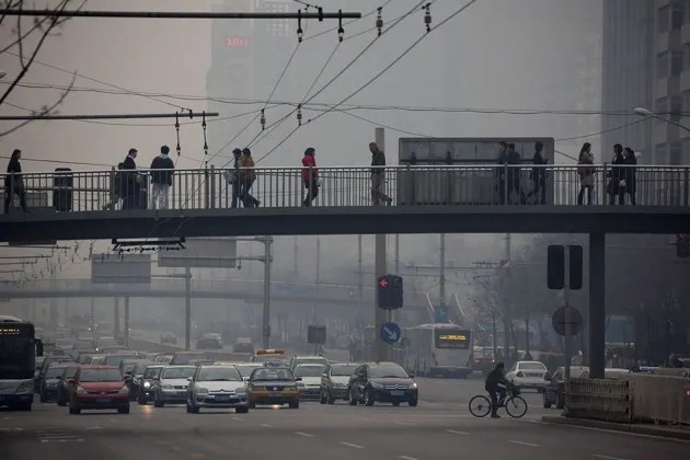 Traffic moves along a street as pedestrians walk on an overpass shrouded in haze in Beijing