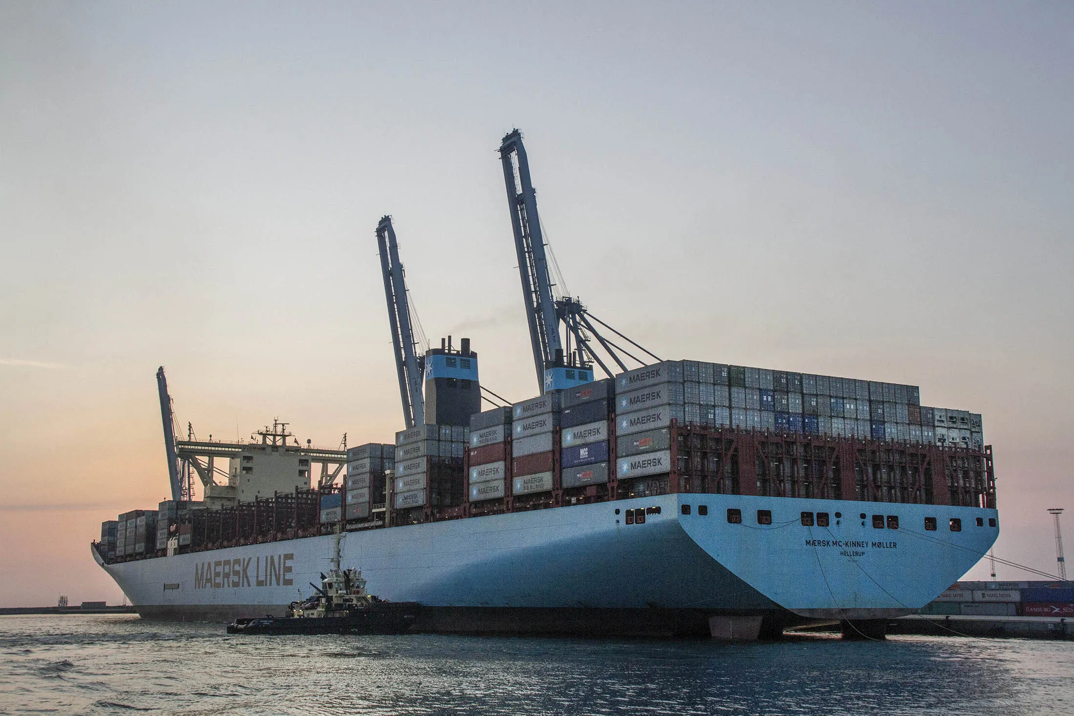 Shipping containers stand aboard the Maersk Mc-Kinney Moller Triple-E Class container ship, operated by A.P. Moeller-Maersk A/S, as it is guided to the dockside by tugboats early morning at the port of Aarhus, Denmark, on Monday, July 28, 2014.
