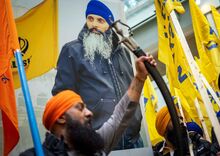 A poster with a photo-portrait of Hardeep Singh is held aloft by protestors bearing yellow Khalistan flags .