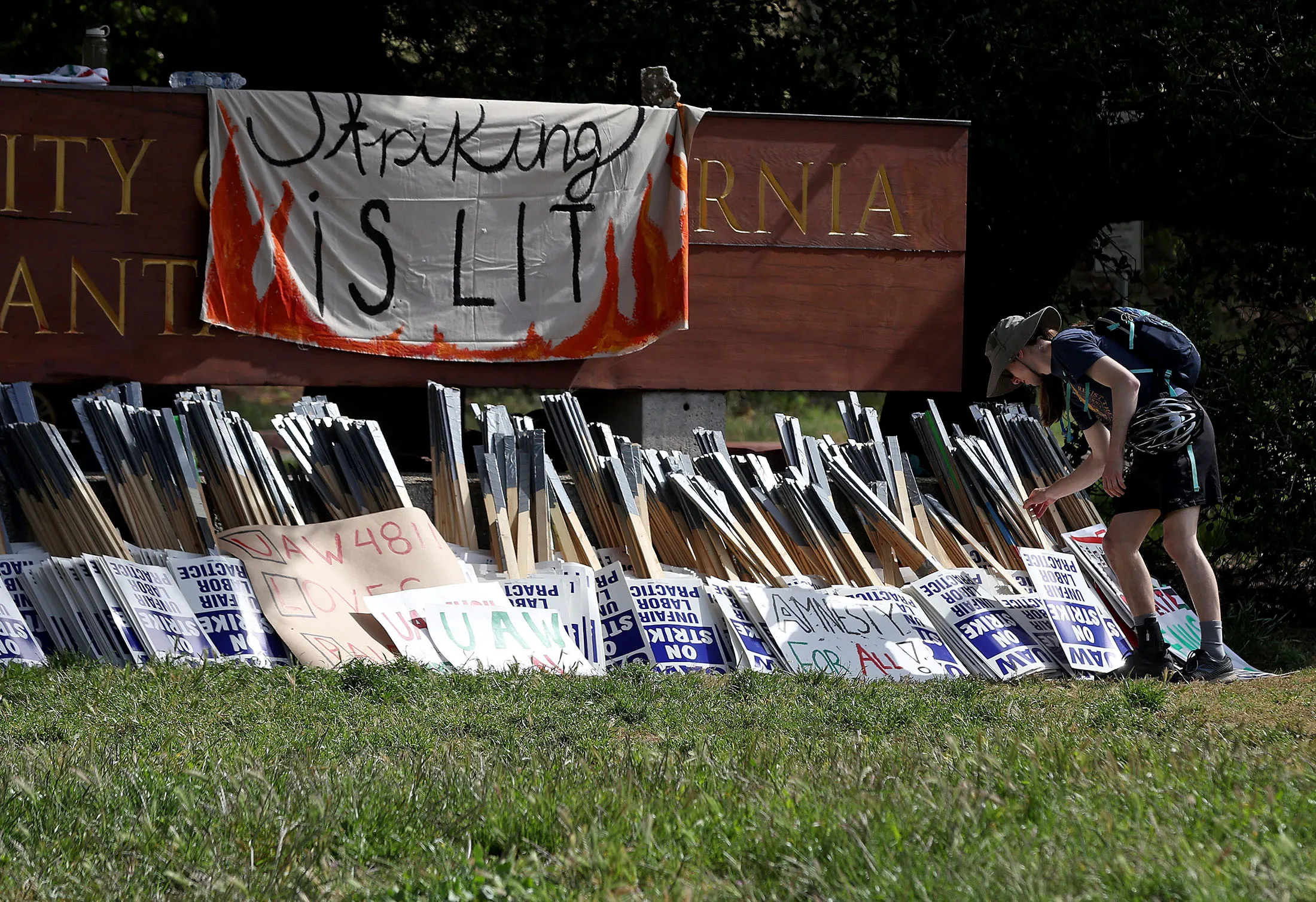 A UC&nbsp;Santa Cruz student worker grabs a sign from a pile to picket in front of the&nbsp;campus on May 20.