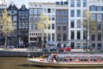 A canal tour boat passes two Tesla Inc. Model 3 electric automobiles at a charging station in Amsterdam, Netherlands.