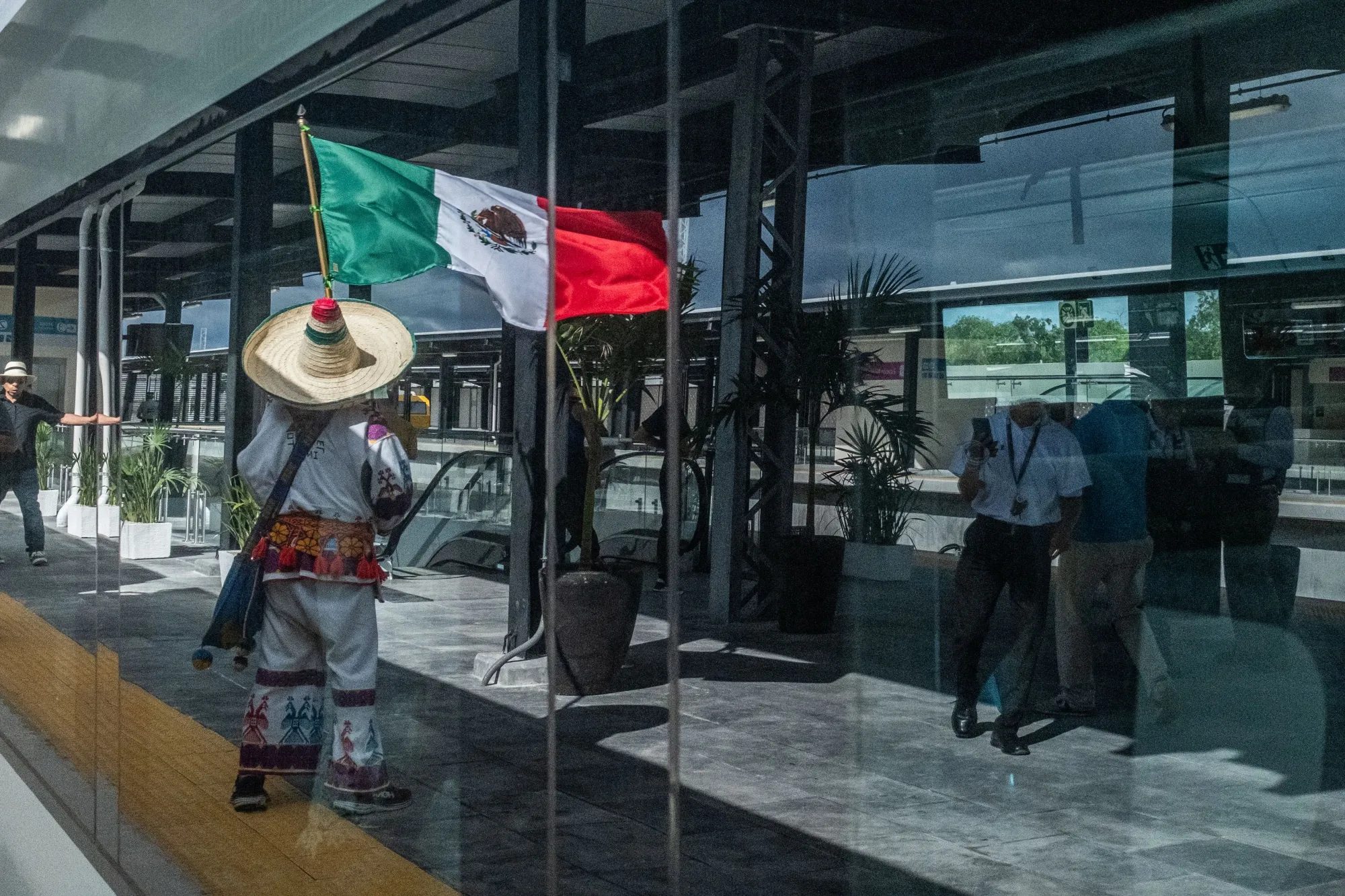 A passenger holding a Mexican flag is reflected in the window of the Maya Train,&nbsp;one of the flagship initiatives on which Andres Manuel Lopez Obrador has spent big in the final year of his presidential term.