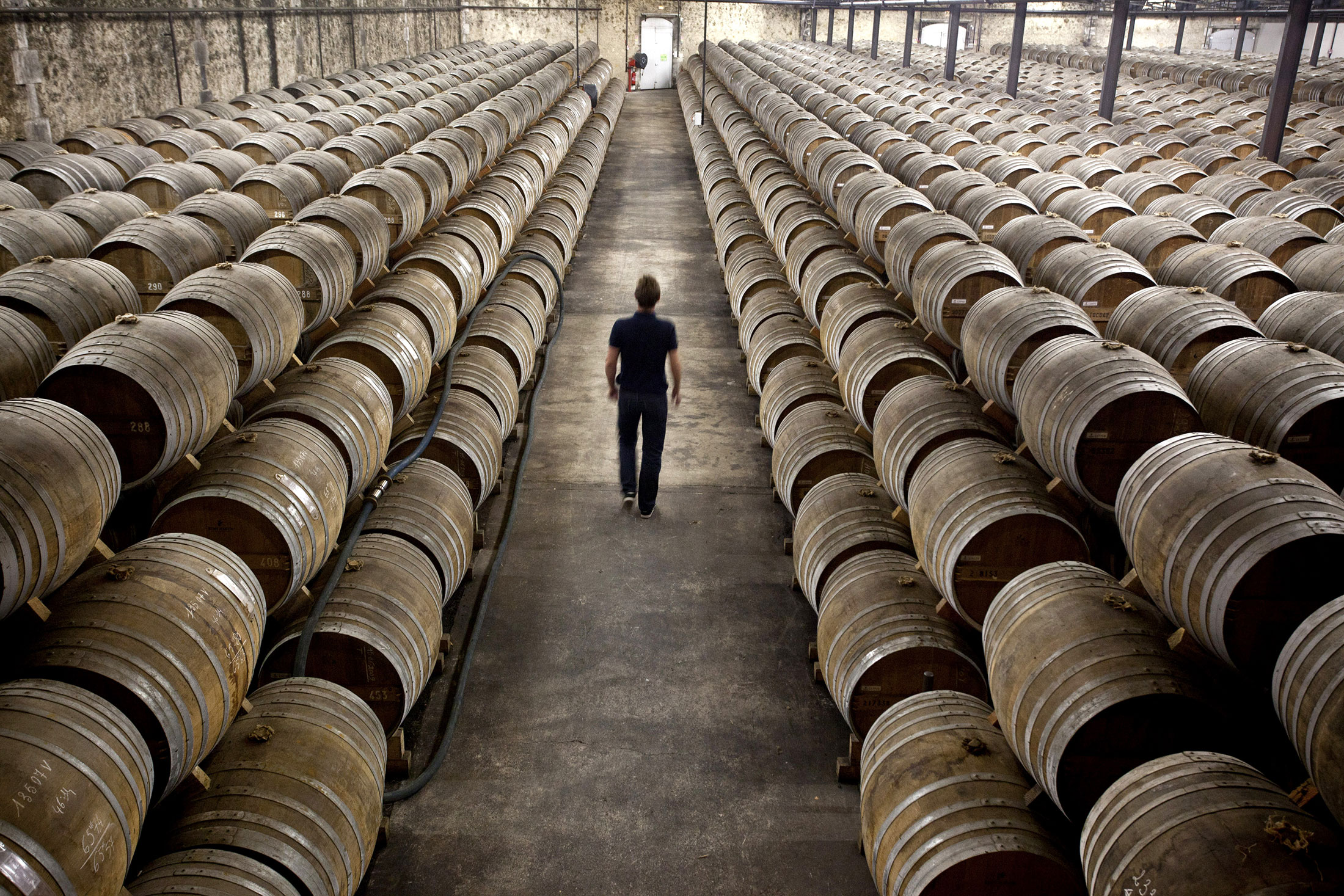 An employee walks between barrels of Remy Martin Fine Champagne Cognac, laid to age in a cellar at the Remy Cointreau SA headquarters in Cognac.
