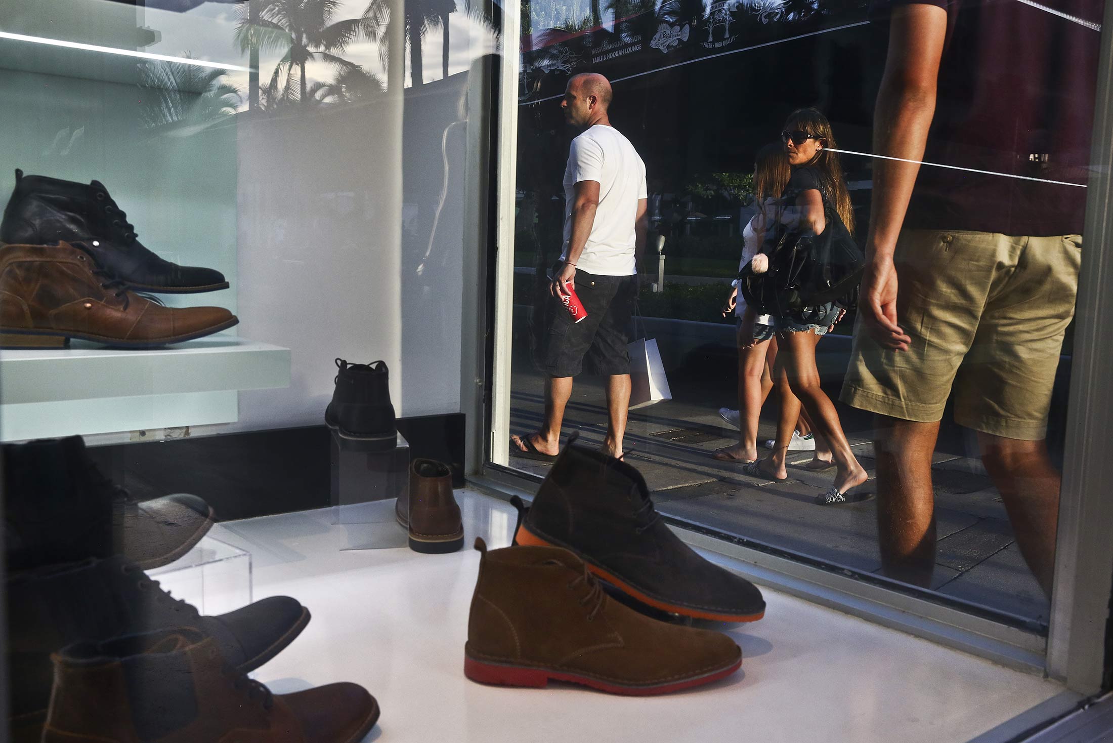 Shoppers and pedestrians pass in front of a store window displaying shoes for sale at the Lincoln Road Mall in Miami Beach, Florida, U.S., on Wednesday, Sept. 21, 2016. The Conference Board is scheduled to release consumer confidence data on Sept. 27.
