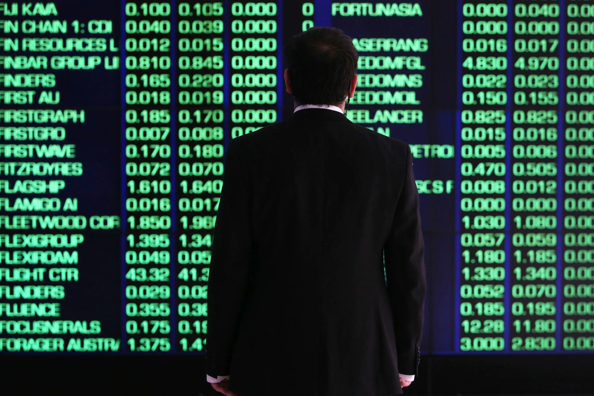 A man looks at an electronic board displaying stock information at the Australian Securities Exchange.