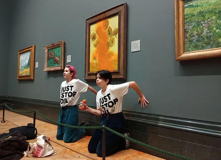 In a handout photo from Just Stop Oil, two&nbsp;protesters glue themselves to the wall at the National Gallery in London after throwing&nbsp;tinned soup at Vincent Van Gogh's famous 1888 work Sunflowers in October.&nbsp;