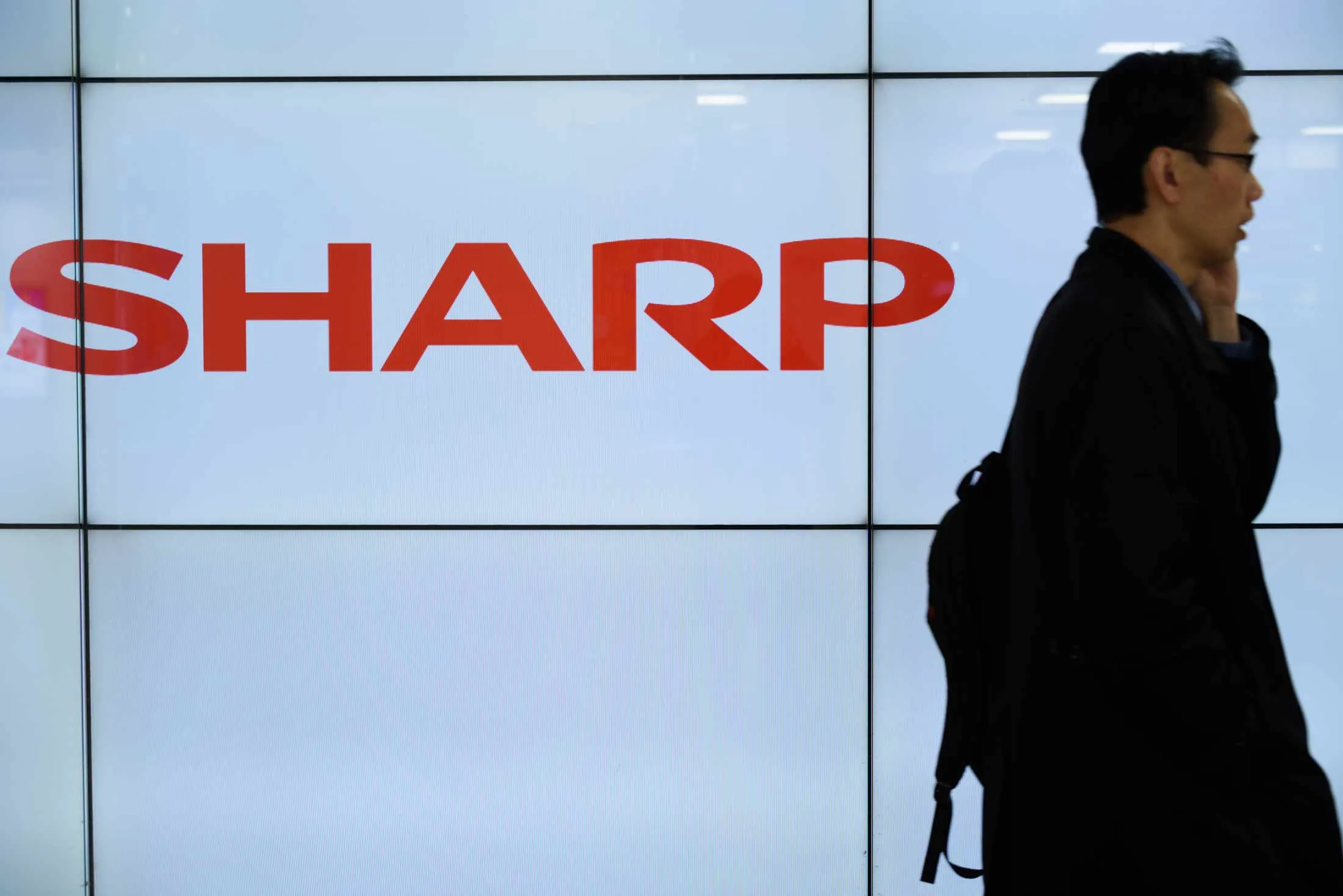 A pedestrian walks past a Sharp Corp. liquid-crystal display in Tokyo, Japan, on Thursday, January 21, 2016.
