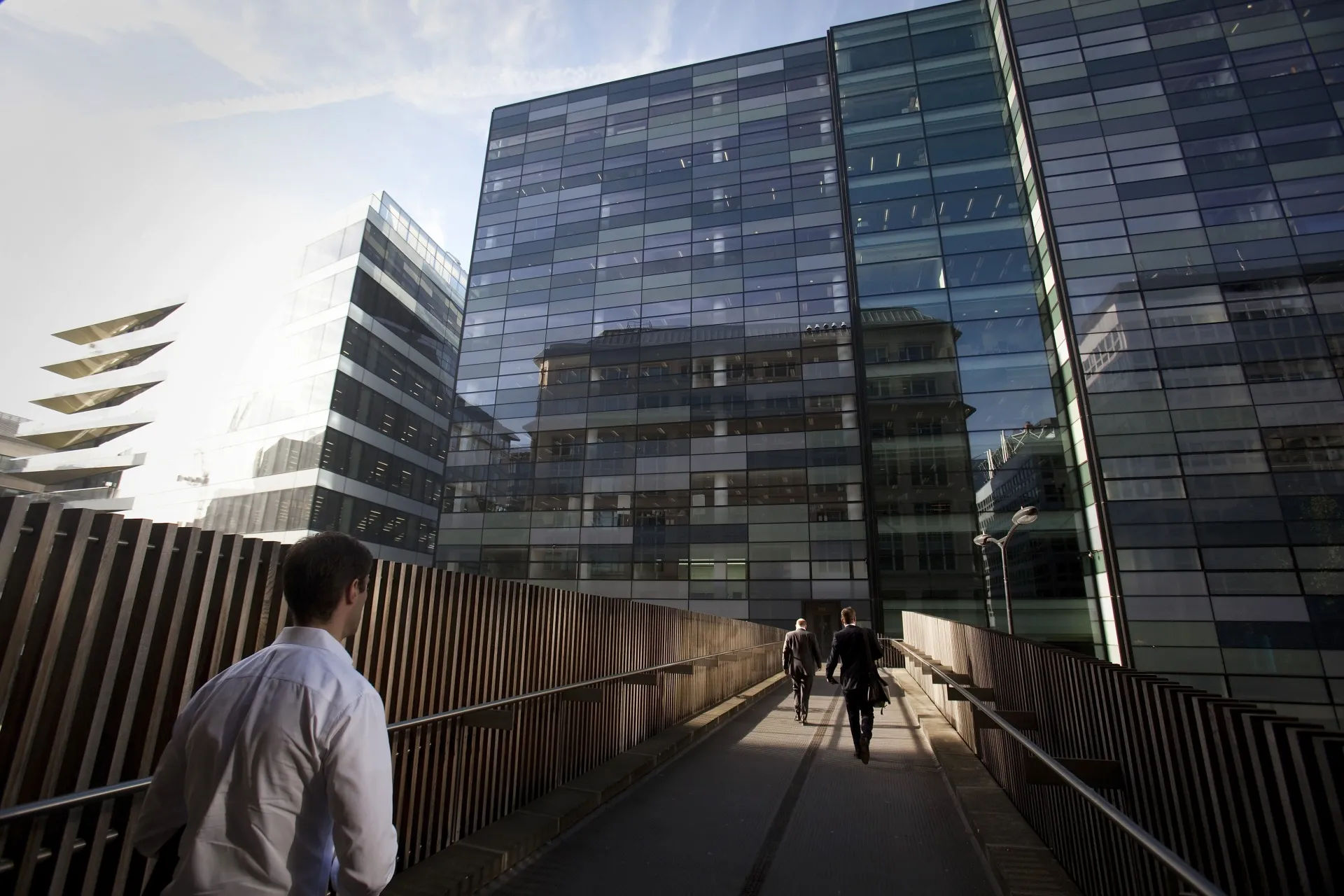 Pedestrians are seen walking across a bridge at the U.K. headquarters of Nomura Asset Management Ltd, right, part of the Nomura Holdings Inc group, in London, U.K.