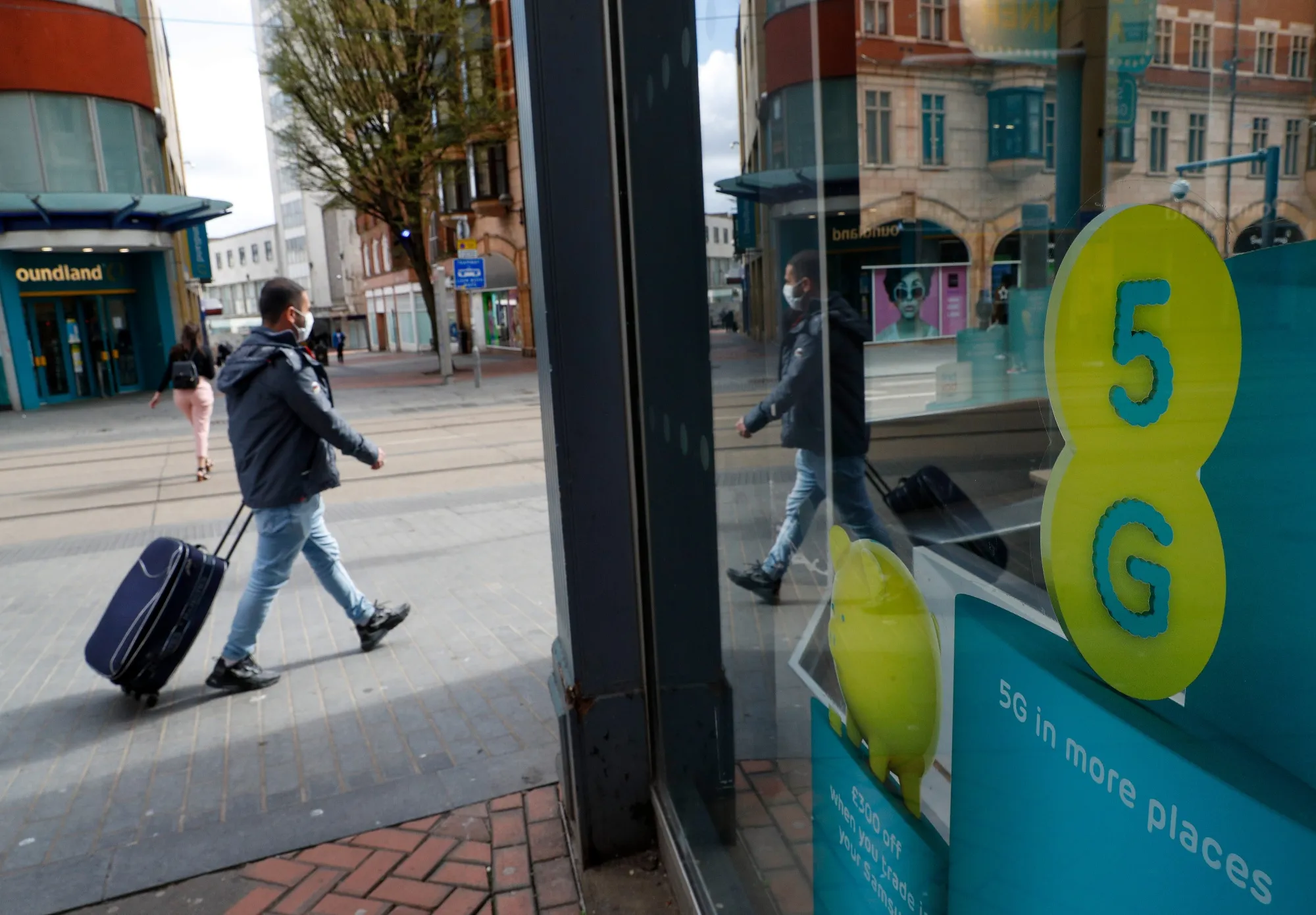 A pedestrian, wearing a protective mask, walks past an advertisement for 5G network services at an EE store, in Birmingham, U.K.