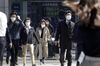 Pedestrians wearing protective masks cross a road in front of an electronic stock board outside a securities firm in Tokyo, Japan.