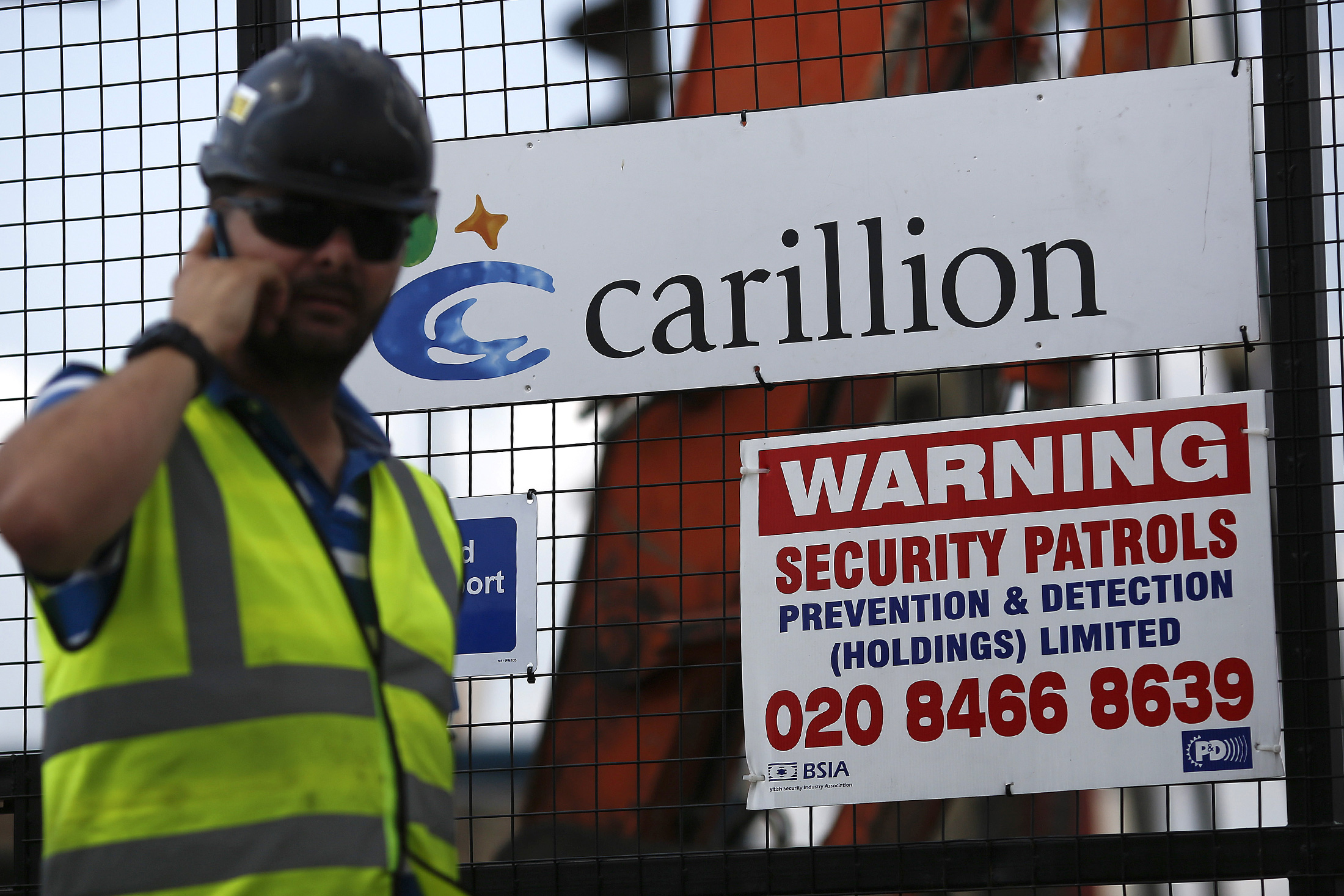 A worker uses a mobile phone outside the gates of a construction site for new apartment blocks built by Carillion Plc in the Canning Town district of London, U.K., on Friday, July 25, 2014. Balfour Beatty, the U.K. construction company whose chief quit in May after predicting a profit drop, is in merger talks with rival Carillion to form the country's biggest builder with a market valuation of about 3 billion pounds ($5 billion).

