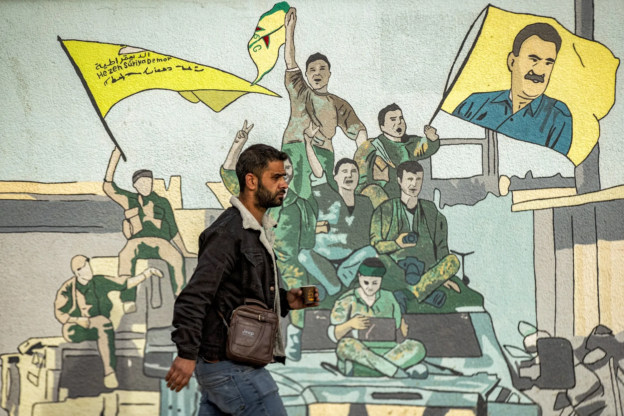 A man walks past a mural showing supporters of the Syrian Democratic Forces, and&nbsp;a flag depicting Abdullah Ocalan in Qamishli , Syria, on Dec. 16.&nbsp;