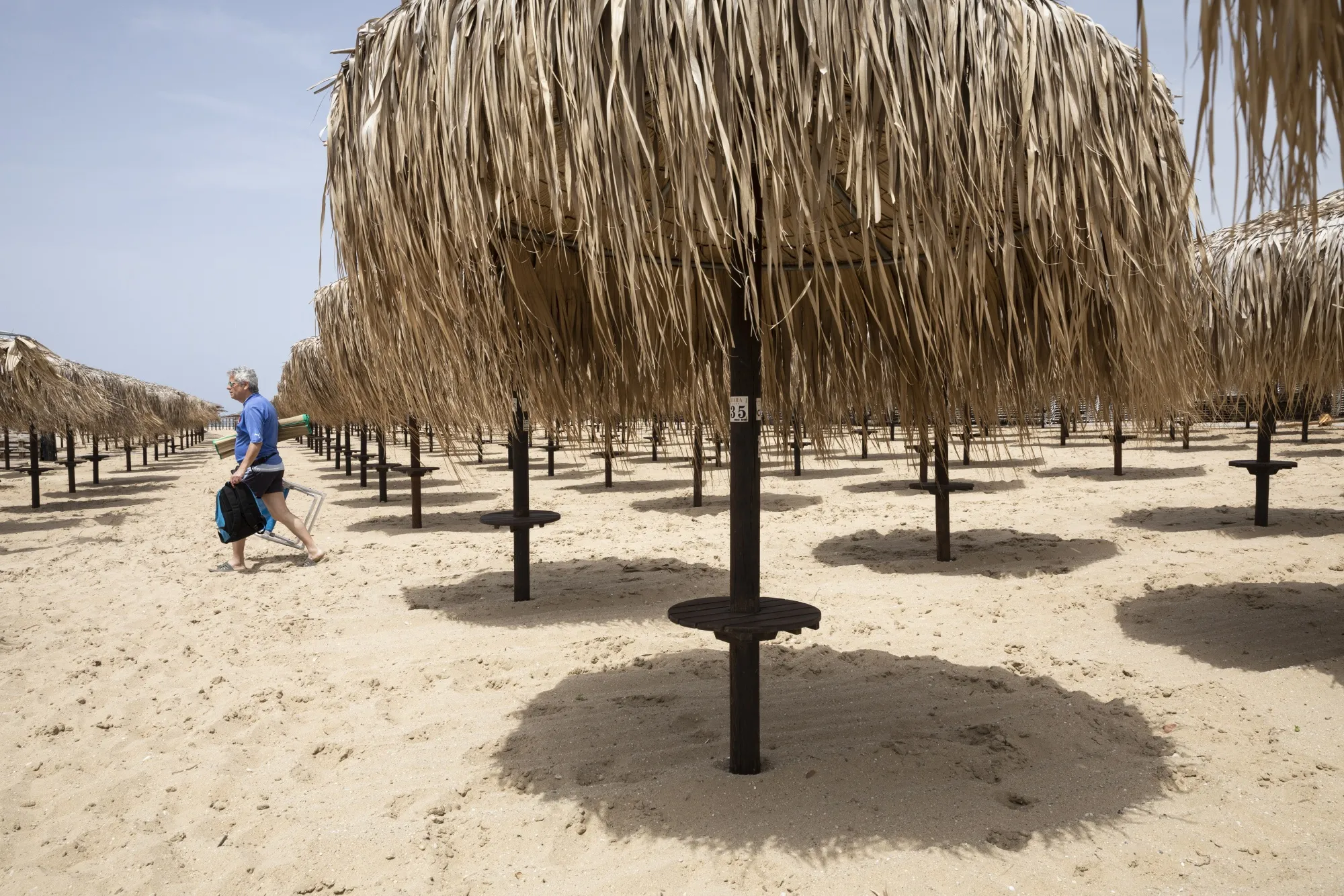 A man passes across rows of empty beach umbrellas of a temporarily closed beach bar in Nea Iraklia, Halkidiki, Greece.