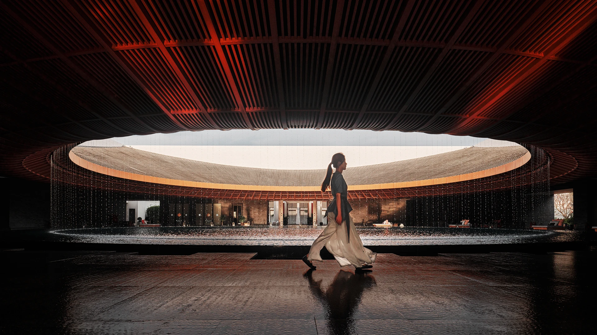 A person with a ponytail walking past a large, circular indoor courtyard under a dark, wooden slatted ceiling with a central oculus opening to the sky. Water trickles down around the circumference of the circular opening into a shallow pool below.